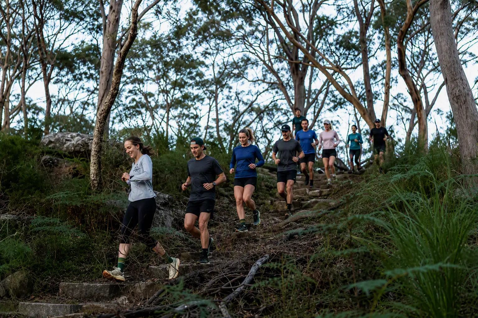 A group of trail runners descending a rocky bush track at Manly Dam